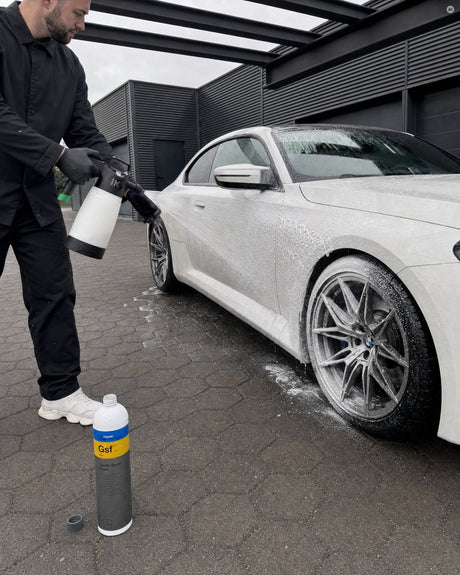 Daniel trägt mit dem iK Foam Pro 2 Pumpschaumsprüher Schaum auf den nassen Lack eines weißen BMW M2 auf — gezeigt im Artikel