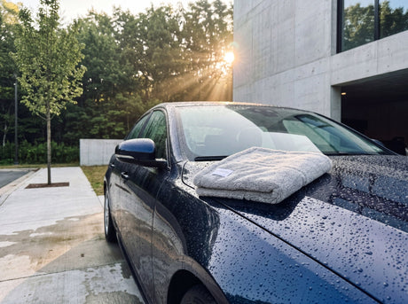 Auto trocknen ohne Kratzer — frisch gewaschene midnight blue Limousine mit 'Aqua' Twisted Loop 1500 GSM Trockentuch auf Motorhaube, Morgenlicht am Forecourt